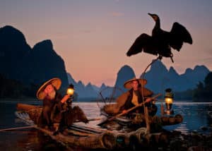 men in large hat rowing on water at sunset