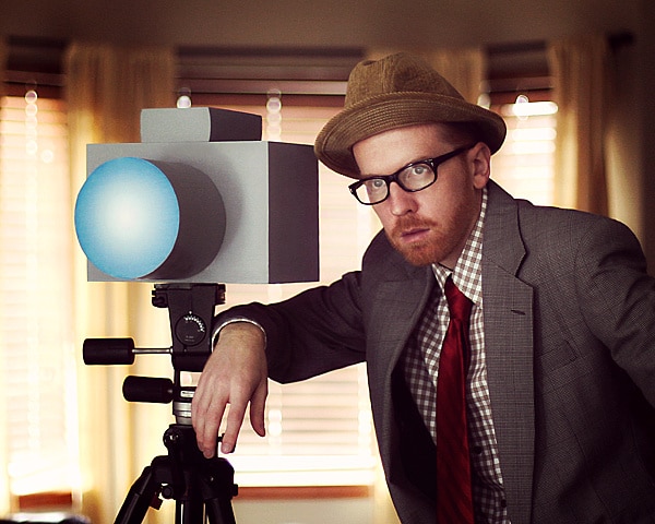 Man standing next to large fake camera on tripod