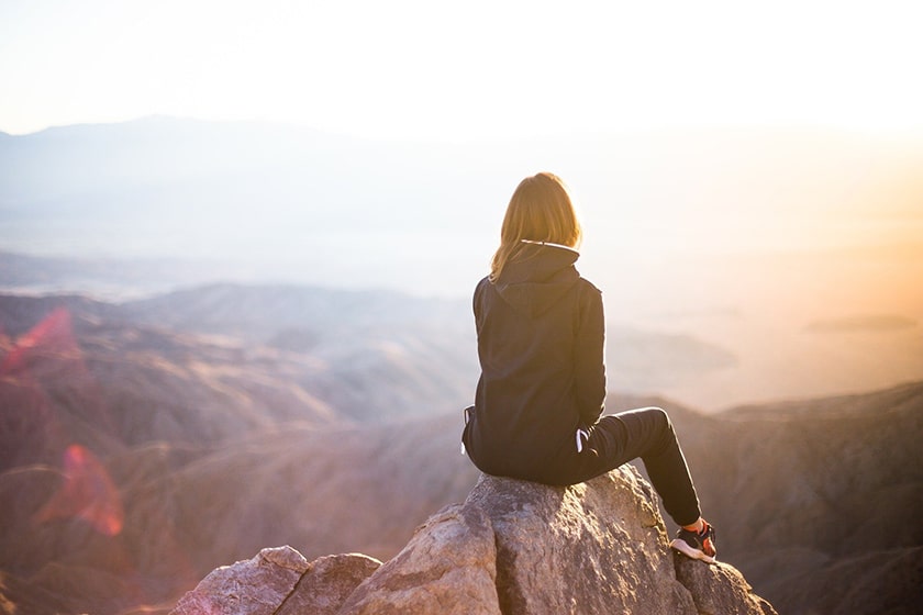 woman sitting on mountaintop at sunset