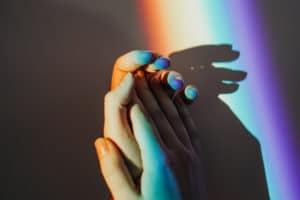 two clasped hands in beam of rainbow light.