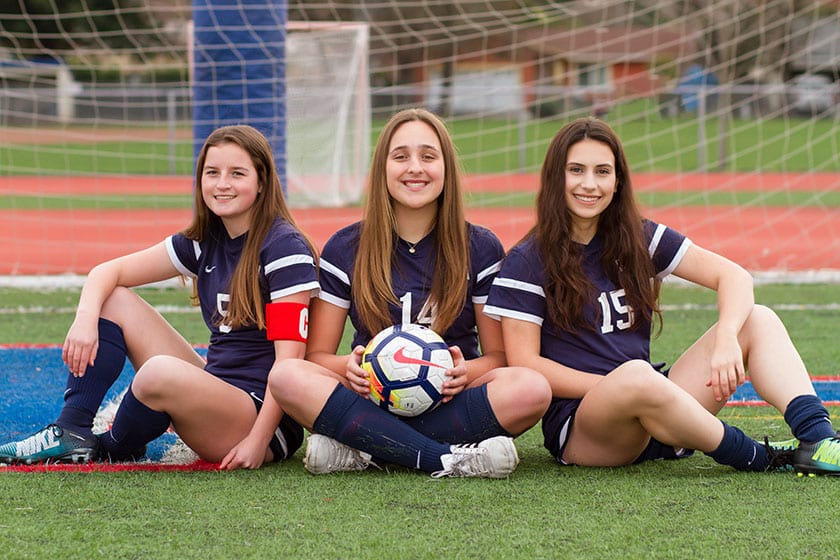 three female soccer players sitting on field