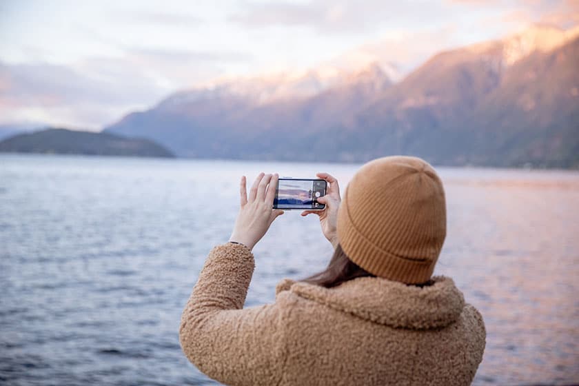 woman taking photo with cell phone at coast