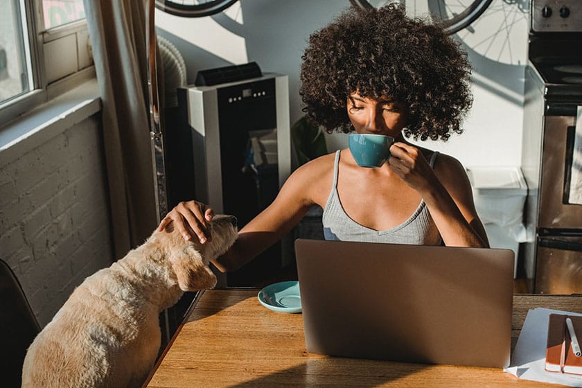 woman at desk drinking tea and petting dog