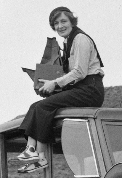 Portrait of Dorothea Lange atop an automobile holding her camera