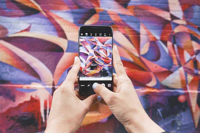 hands using mobile phone to photograph mural