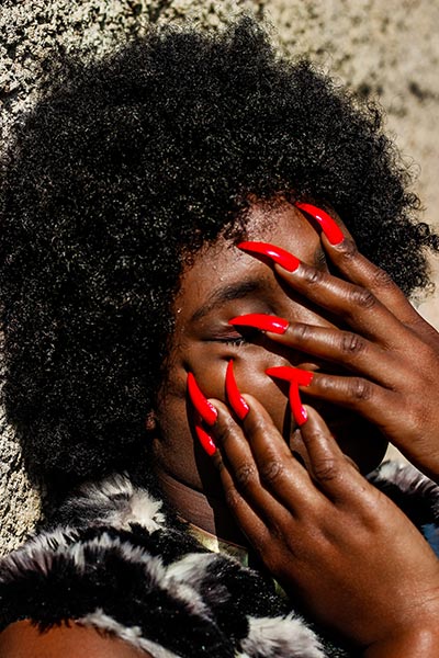 black woman with her hands and long red fingernails covering her face