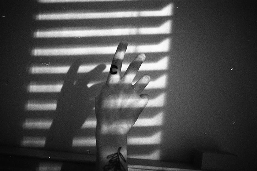 black and white image of a hand lit through slitted blinds