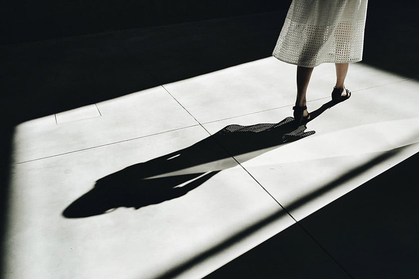 shadow of a woman wearing an eyelet dress in a pocket of window light on the ground
