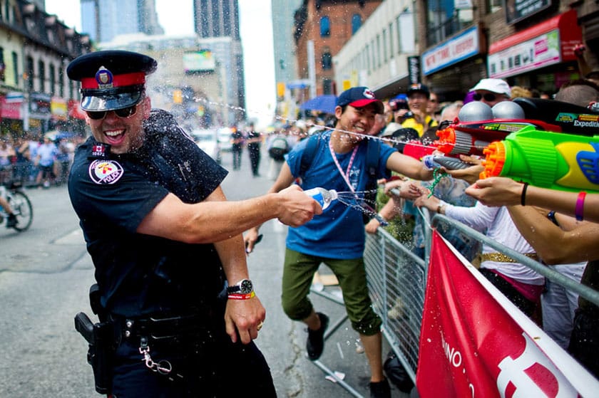a crowd playfully squirting a smiling police officer with water guns in a street