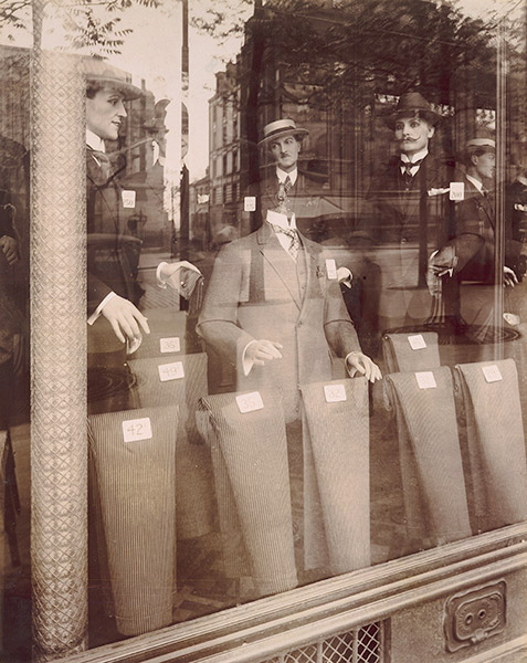 street photograph of a haberdashery shop window, the surrounding buildings reflected in the glass