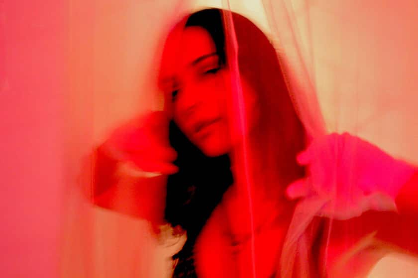 a woman peeking through gauzy curtains in reddish light