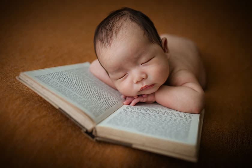 baby posed with arms crossed on an open book, their head resting on their arms