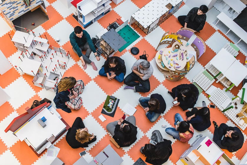 people seated on an orange and white foam tile floor, surrounded by models of modern buildings