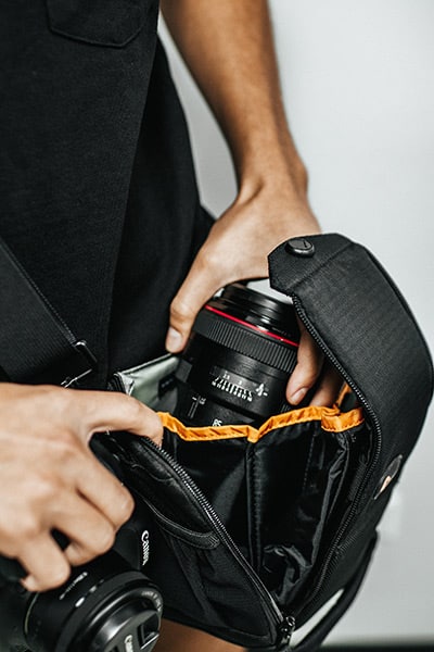 photographer's hands placing a camera lens into a camera bag
