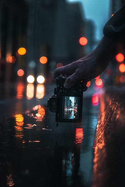 camera held close to the ground on a wet street, with the city scene showing on the digital display of the camera back