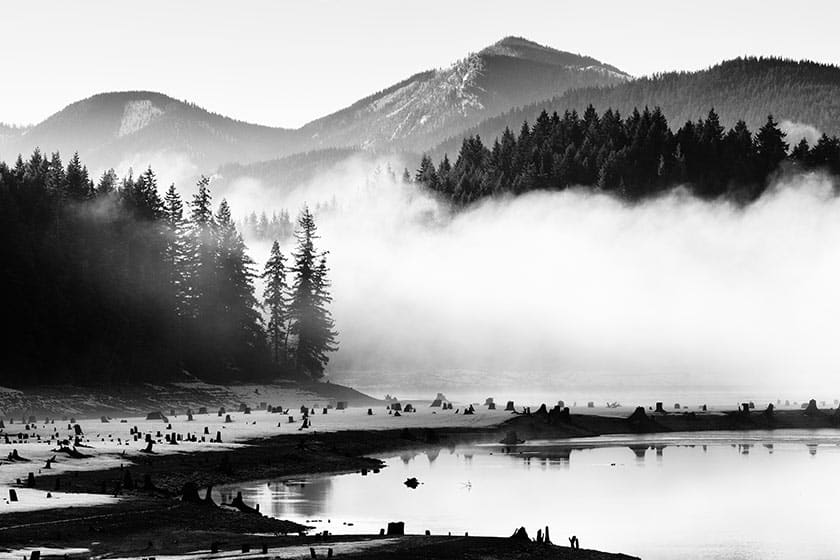 black and white image of a foggy water and mountain scene