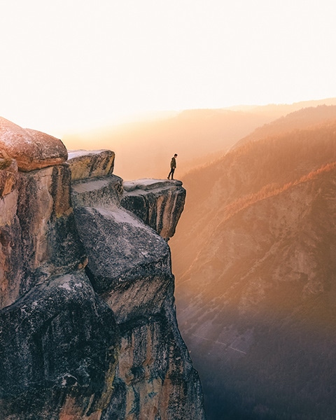 landscape image of person on a cliff in the mountains during sunset