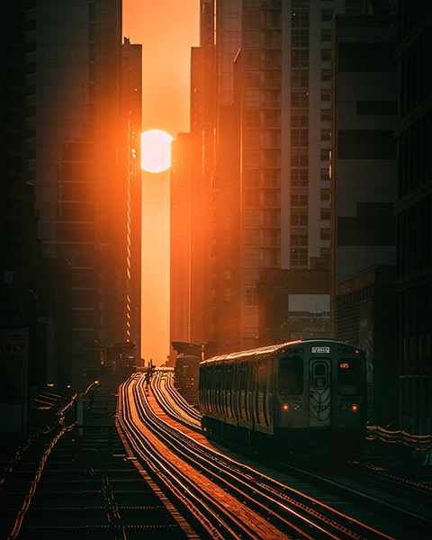 glowing sun setting in an orange sky, its light reflecting on the skyscrapers and train tracks running between them