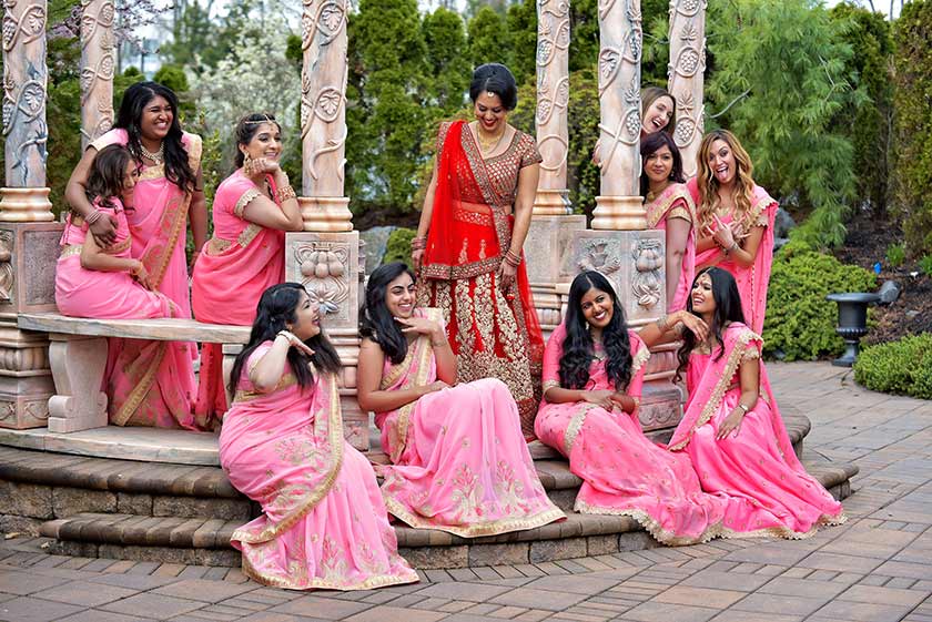 indian bridal party posed seated and standing around a stone structure at the wedding venue