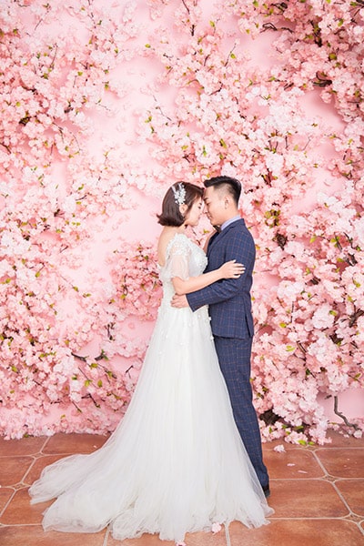wedding portrait of bride and groom standing in front of a pink flower-covered wall
