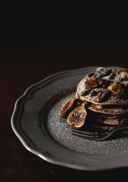 pancakes and figs dusted with powered sugar resting in a grey plate on a black background
