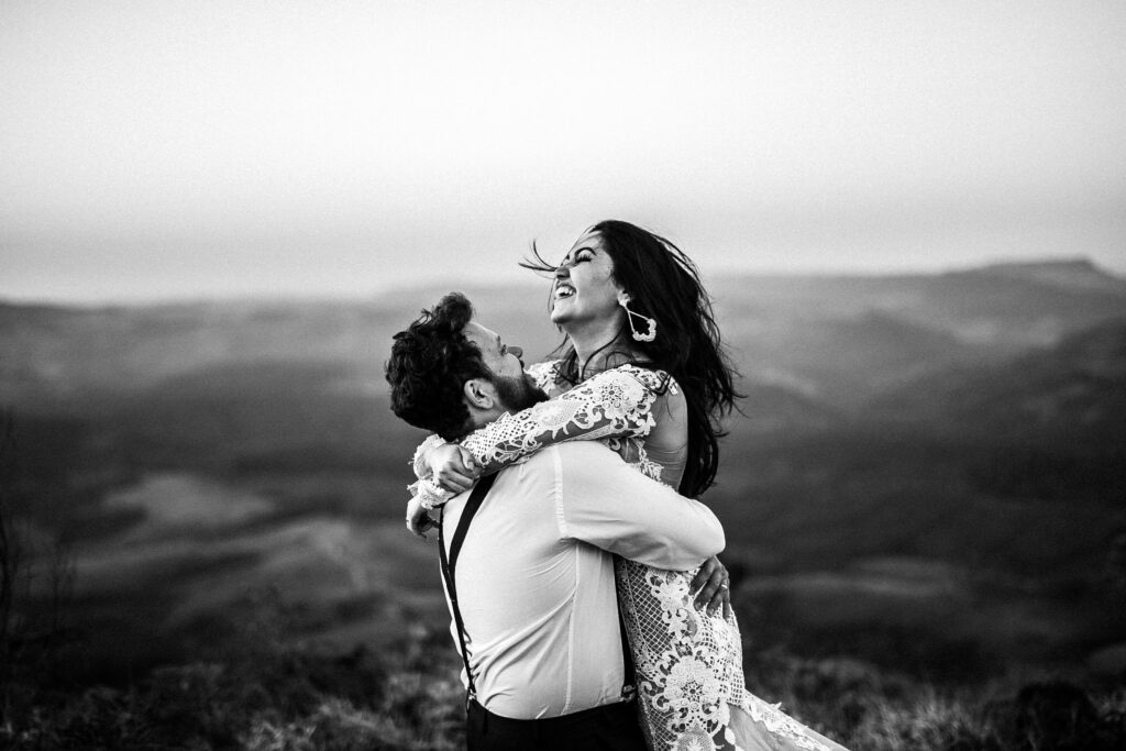 black and white wedding portrait of bride and groom laughing and hugging on a mountain