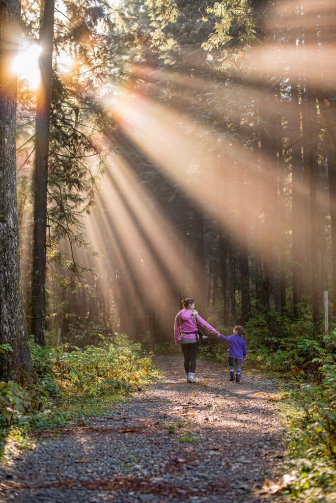 mother and daughter walking in the forest surrounded by rays of light