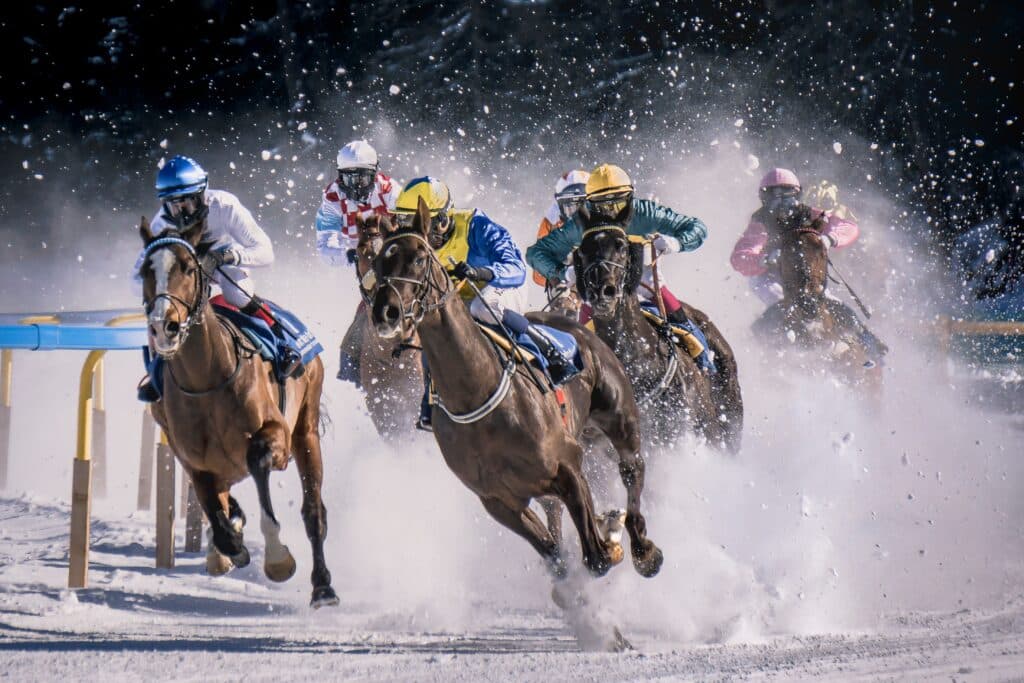 5 horses and riders competing in horse race on icy lake in Sankt Moritz