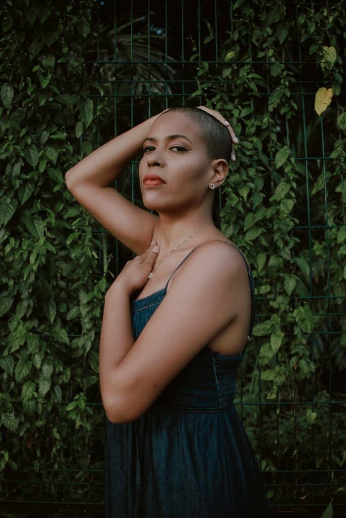 black woman wearing makeup and posed dramatically with raised arm resting on her shaved head