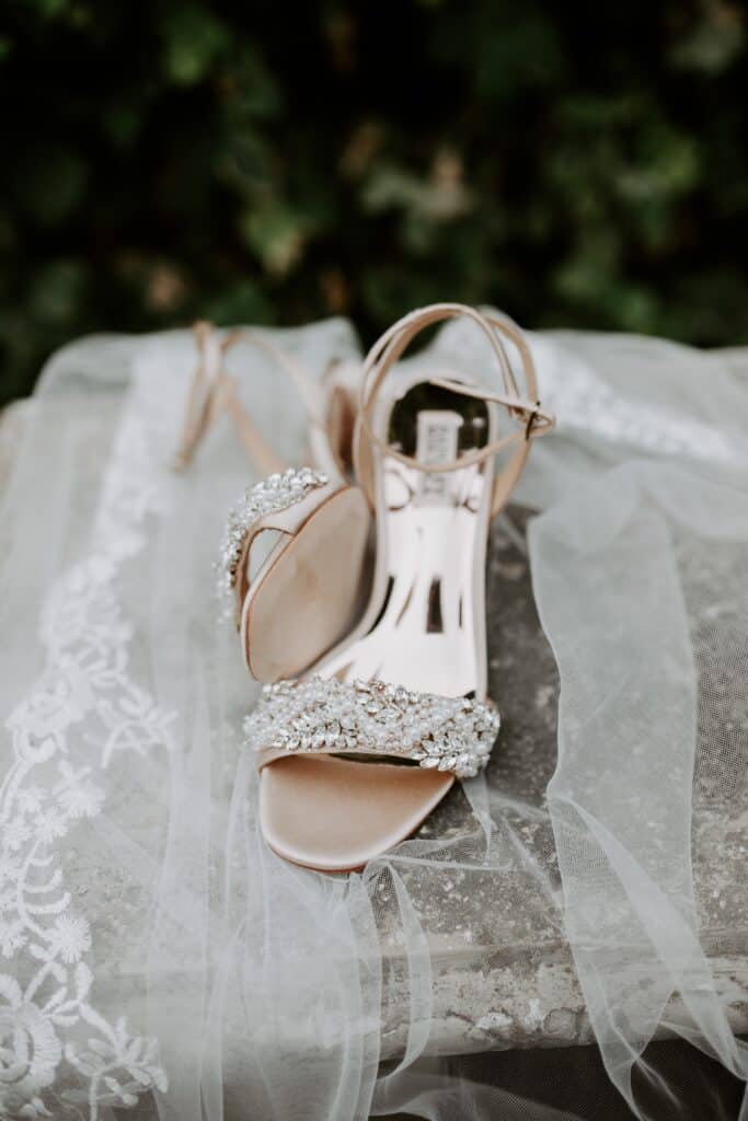 bridal veil with lace trim spread on a stone bench under rose gold shoes studded with crystals