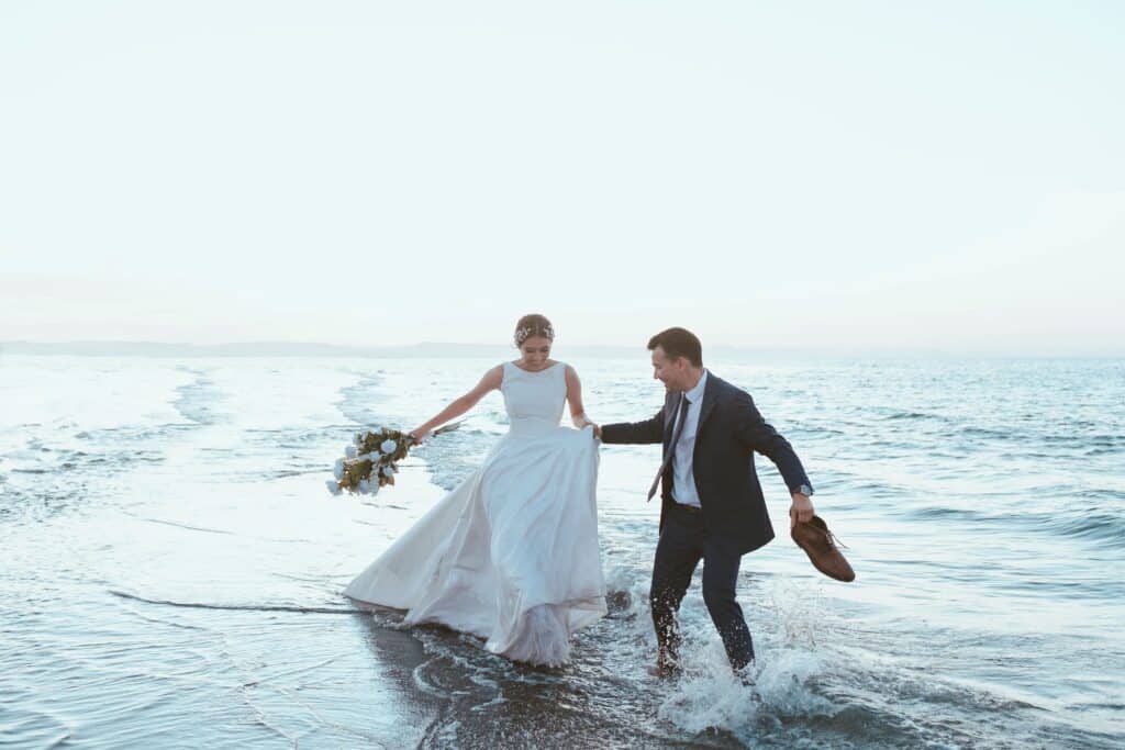 bride and groom splashing through the edge of the ocean in their wedding clothes