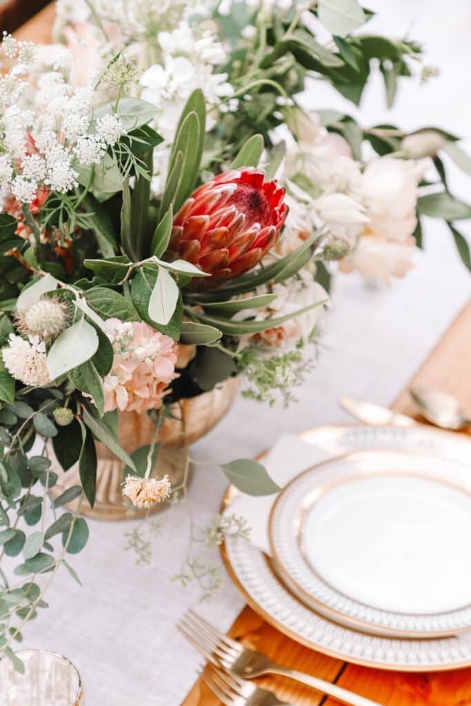 gold vessel holding a floral table arrangement beside gold rimmed white plates