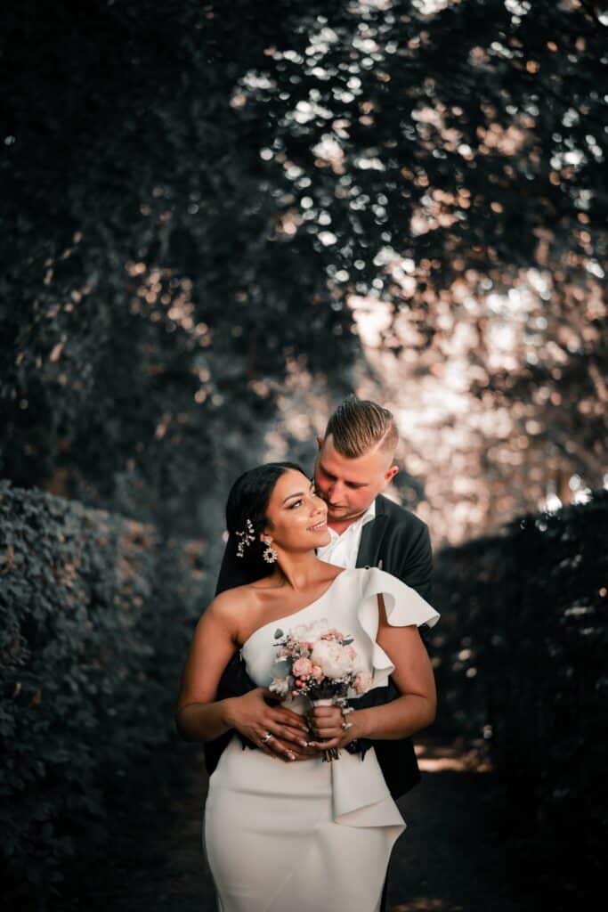 groom hugging bride from behind between the hedges of a garden path
