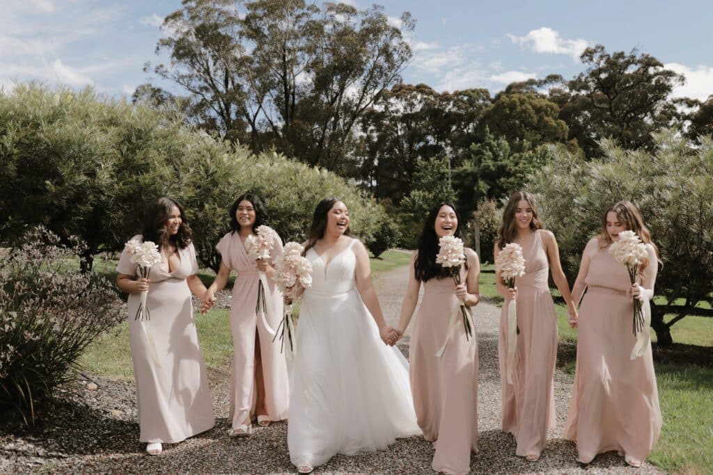 happy bride walking while surrounded by her five laughing bridesmaids