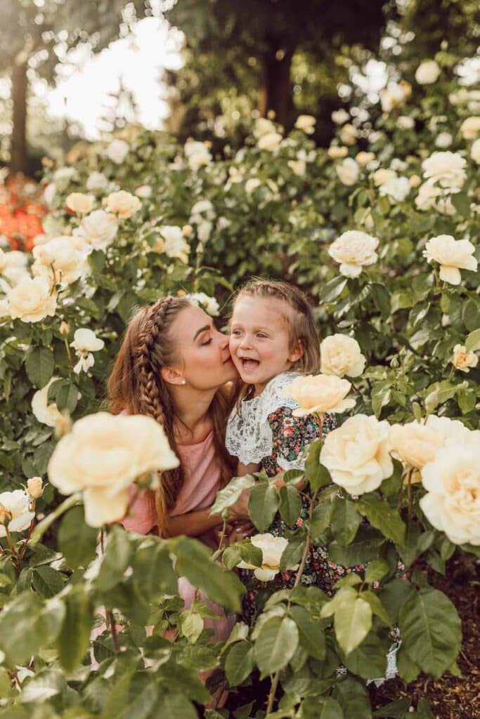 mother and daughter sitting in a patch of pale yellow roses