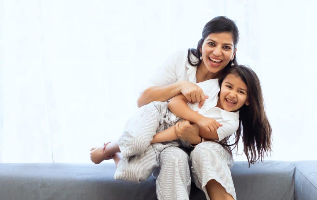 smiling mother hugging laughing daughter across her lap, with large area of negative space to the left of the image