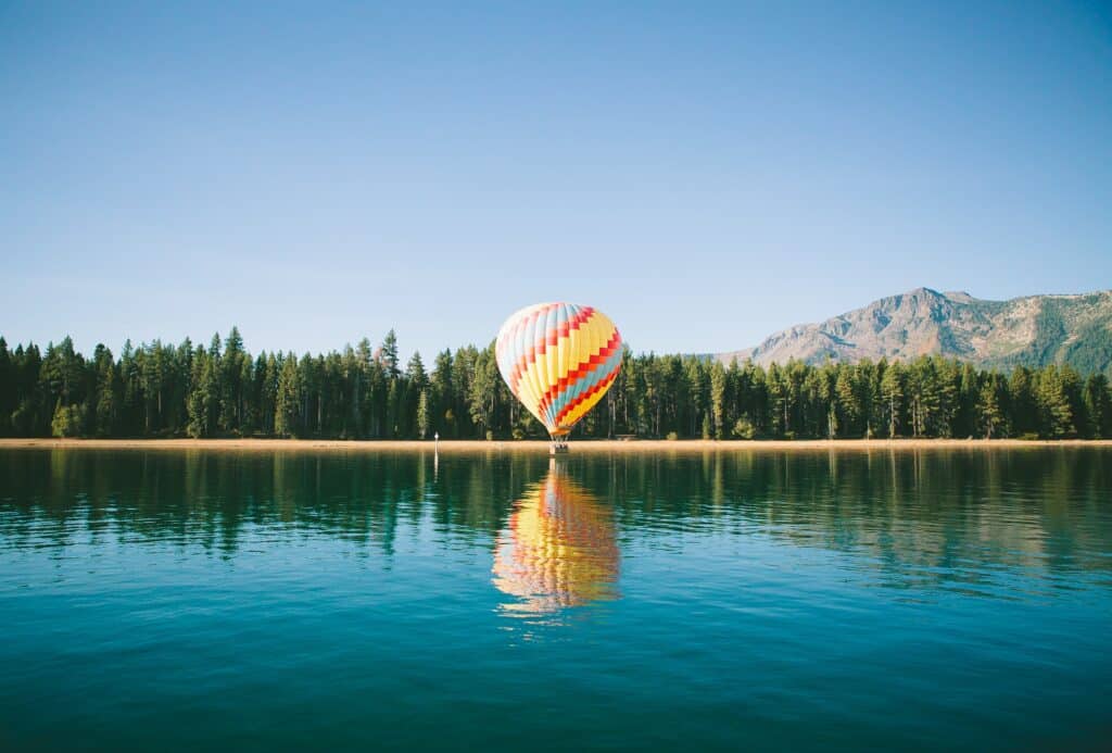 colorful hot air ballon reflecting in the water on the edge of a lake