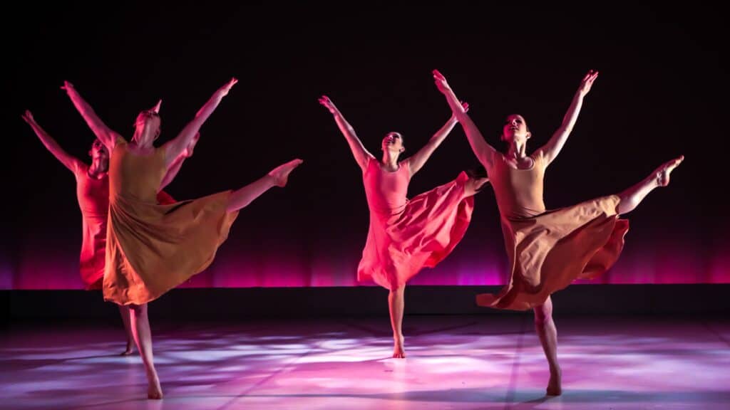 four female dancers kicking a leg in the air in sync on a stage