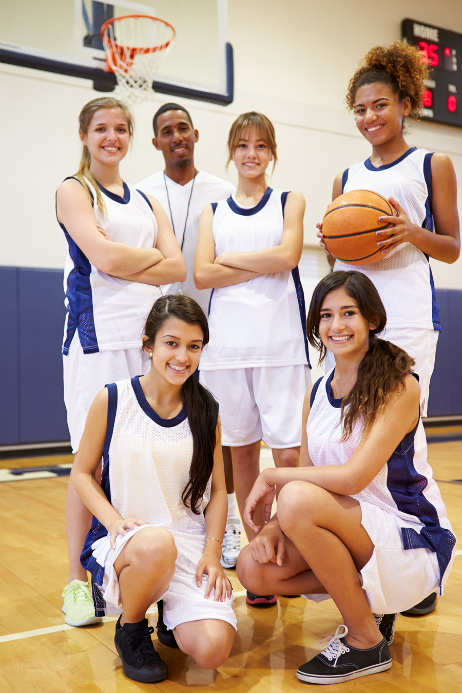 girls basketball team posing with ball and coach under net