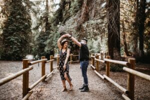 man holding woman by the hand and twirling her on path in a redwood forest