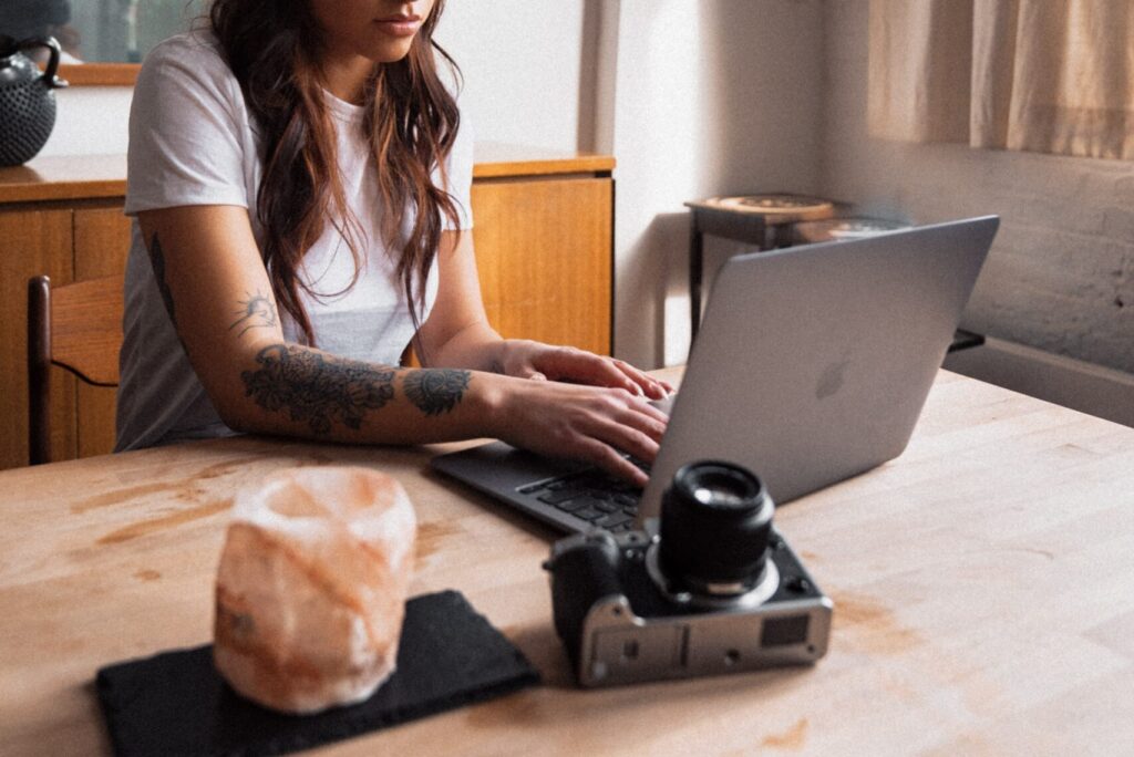 female photographer sitting at wooden table with laptop and camera