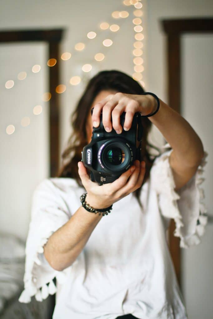 portrait of a photographer wearing a white top and holding their camera in front of their face