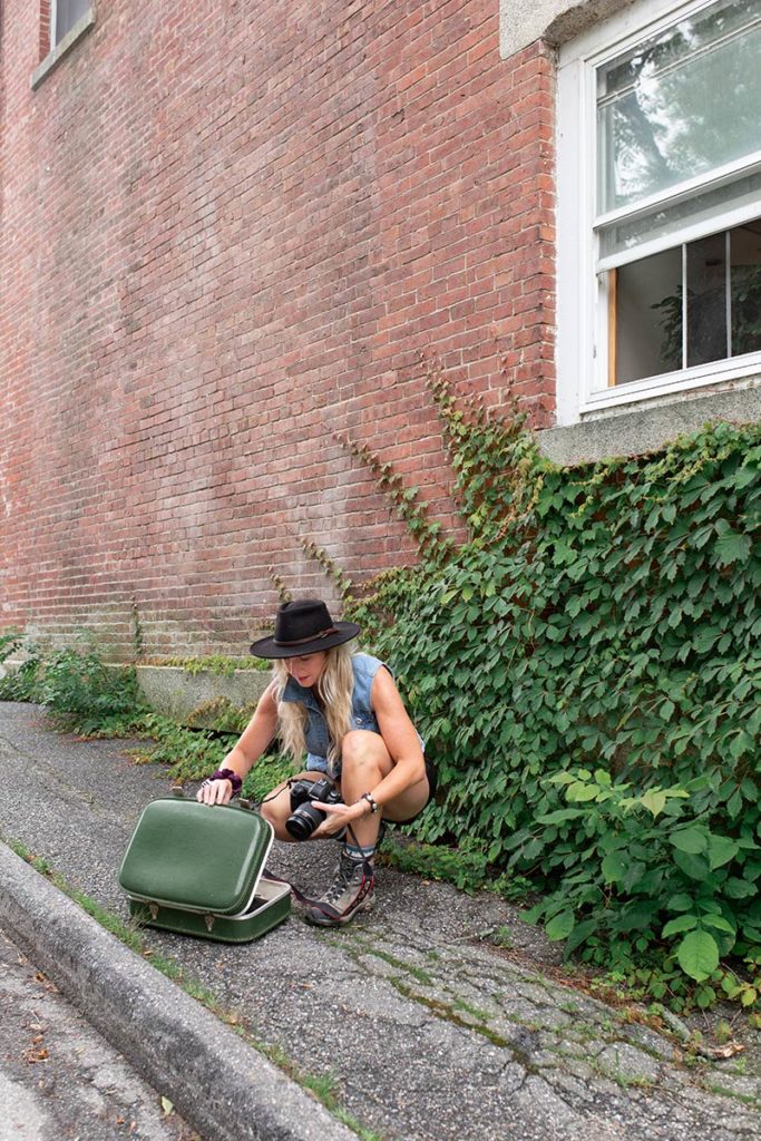 female looking in suitcase on paved sidewalk