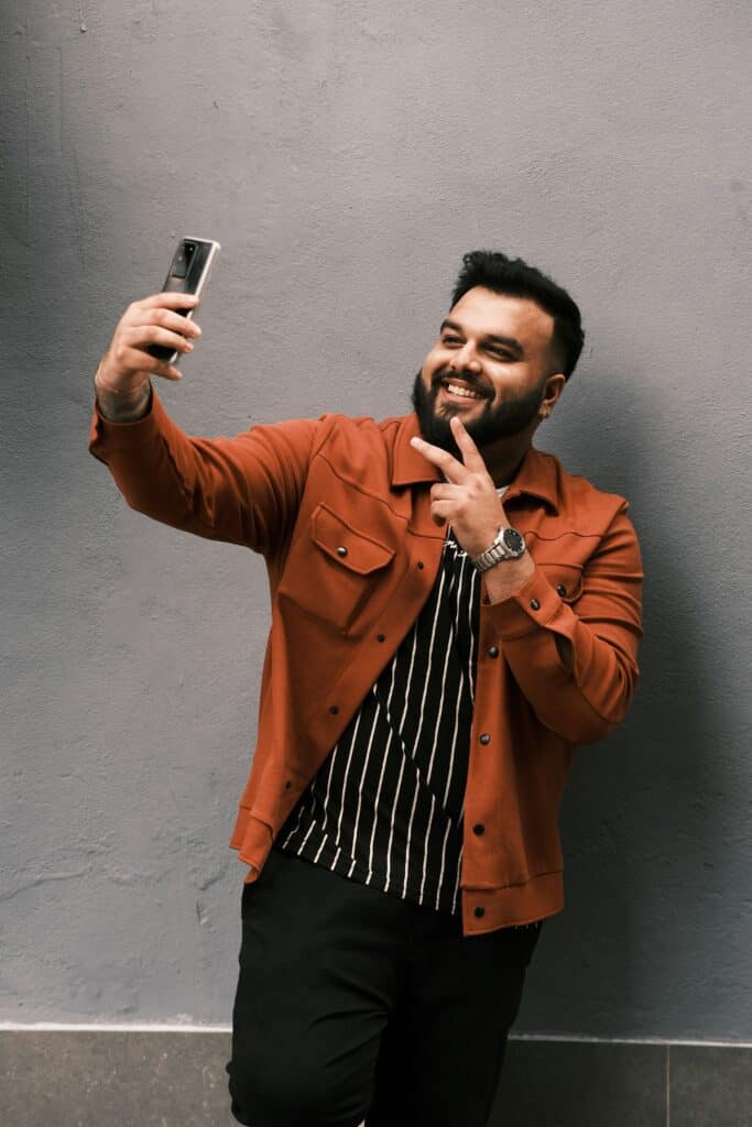 happy man leaning against wall and taking selfie video while making the peace sign