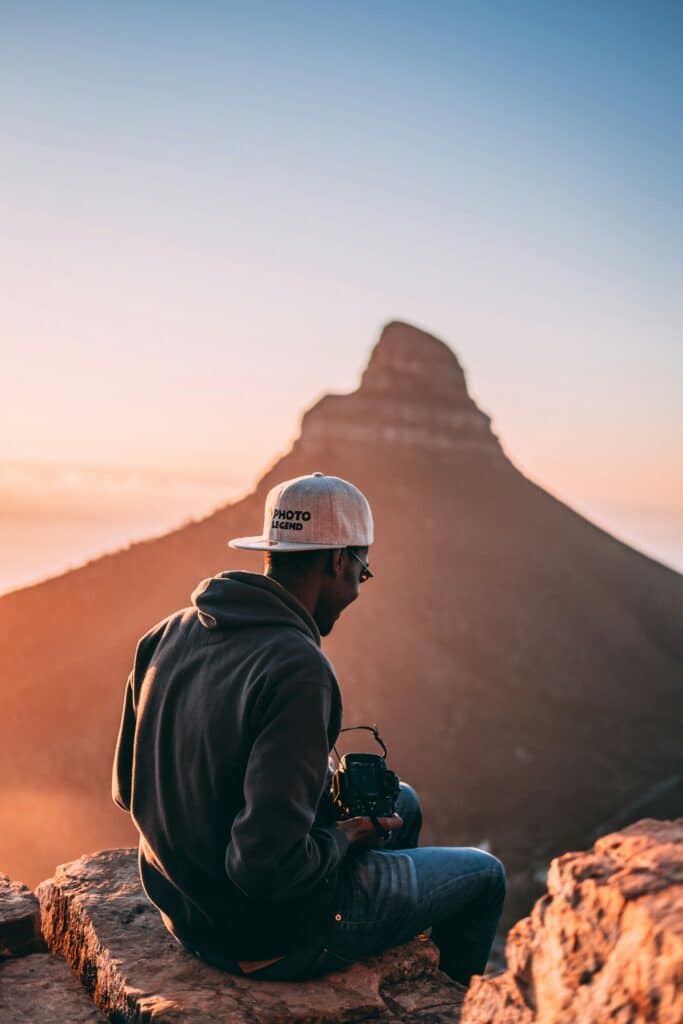 photographer sitting on rock holding camera with mountain in the distance