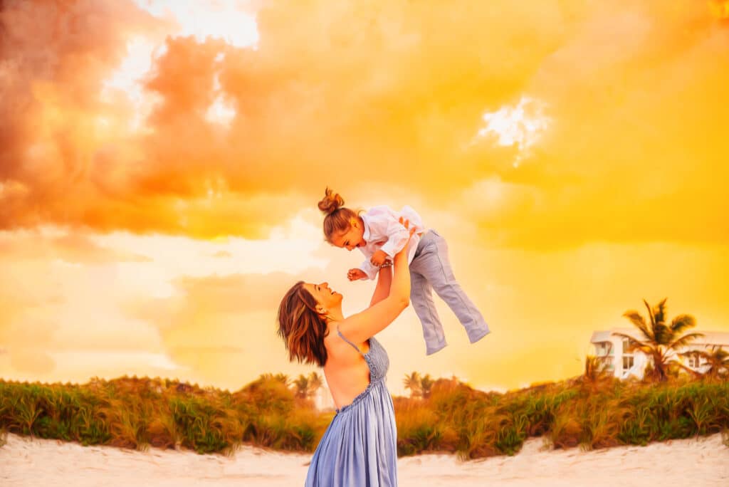 Mommy & Me portrait of mother holding child up in the air above her head while at the beach at sunset. Photographed by JS Portrait Studio Delray Beach