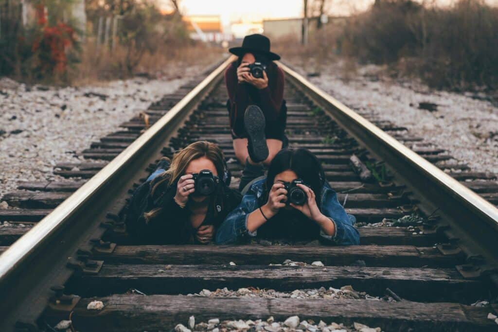 three photographers with cameras on railroad tracks, two on their bellies and one crouching behind them