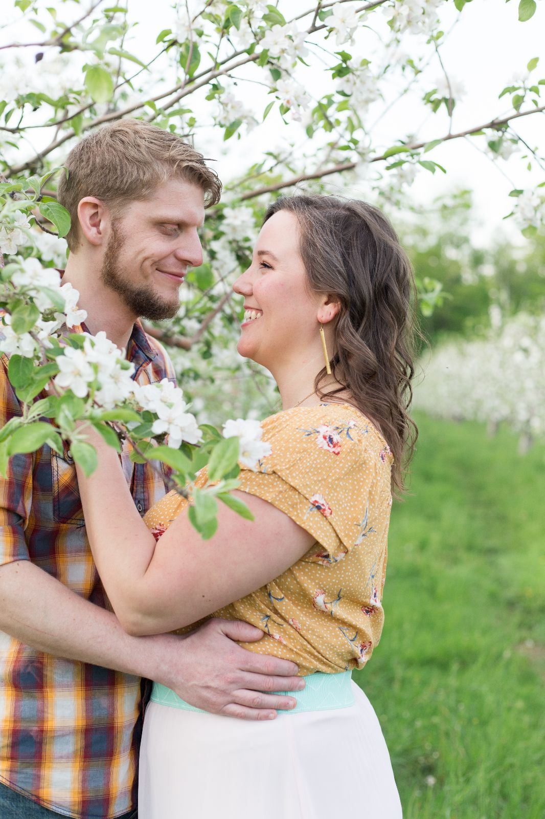 couple facing each other with their arms around each other, surrounded by blooming apple trees in spring