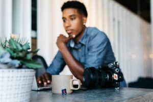 male photographer using laptop at counter beside camera and tea mug
