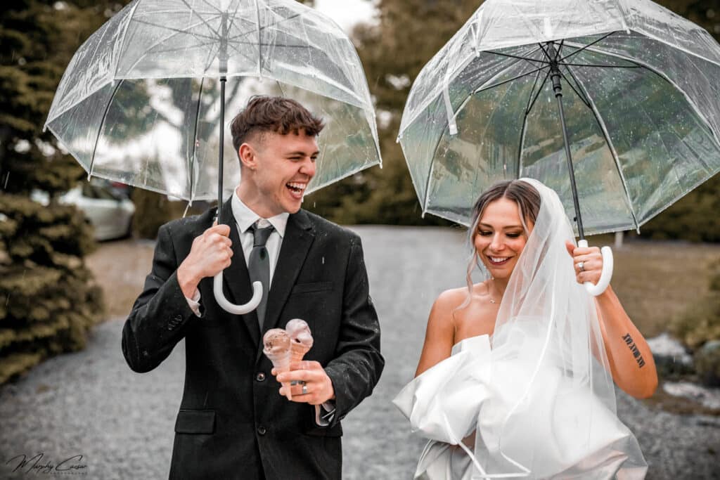 wedding couple walking in rain with umbrellas and carrying ice cream cones. photo by Murphy Caesar
